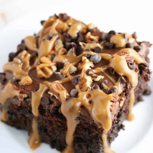 Image of chocolate poke cake topped with chocolate chips, caramel drizzle, and pecans
