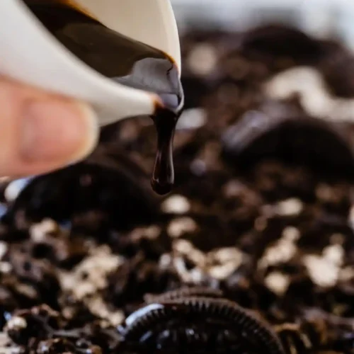 Image of chocolate being poured on top of an oreo poke cake