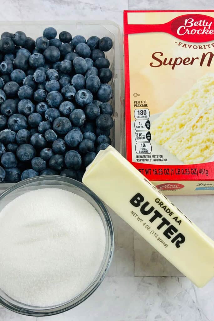 A group of ingredients, including the box of mix, fresh fruit and sugar.
