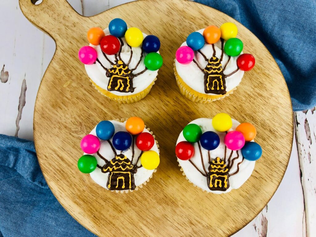 four balloon cupcakes on a wooden serving tray.