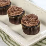 Three cocoa pebbles cupcakes on a white tray.
