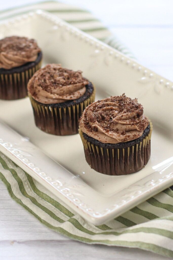 Three cocoa pebbles cupcakes on a white tray.