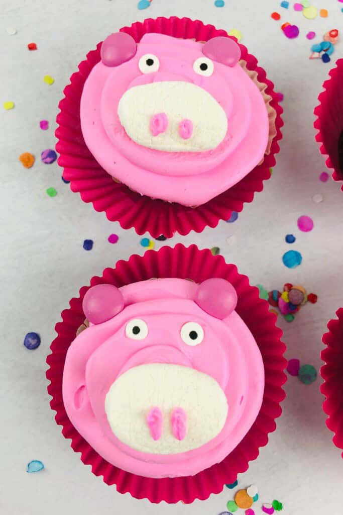 Confetti on a table with pig cupcakes on top.